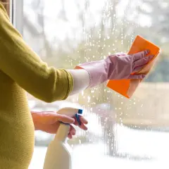 Ciężarna kobieta w rękawiczkach myje okno gąbką i płynem w sprayu.