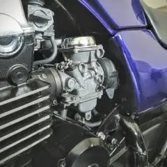 Motocyklowy gaźnik i fragment silnika z fioletowym bakiem.