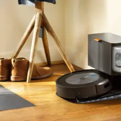 Odkurzacz iRobot Roomba na stacji dokującej, obok butów i stojaka na ubrania.