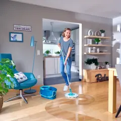 Kobieta myje podłogę mopem ze spryskiwaczem w jasnym salonie.
