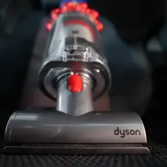 Odkurzacz Dyson na ciemnym tle, widoczna szczotka i pojemnik.