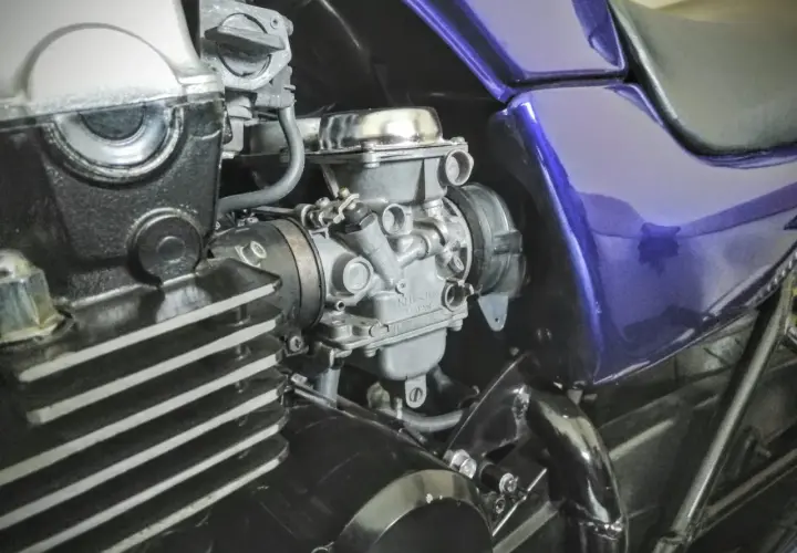 Motocyklowy gaźnik i fragment silnika z fioletowym bakiem.