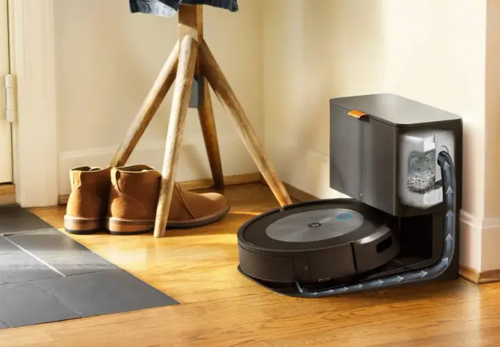 Odkurzacz iRobot Roomba na stacji dokującej, obok butów i stojaka na ubrania.
