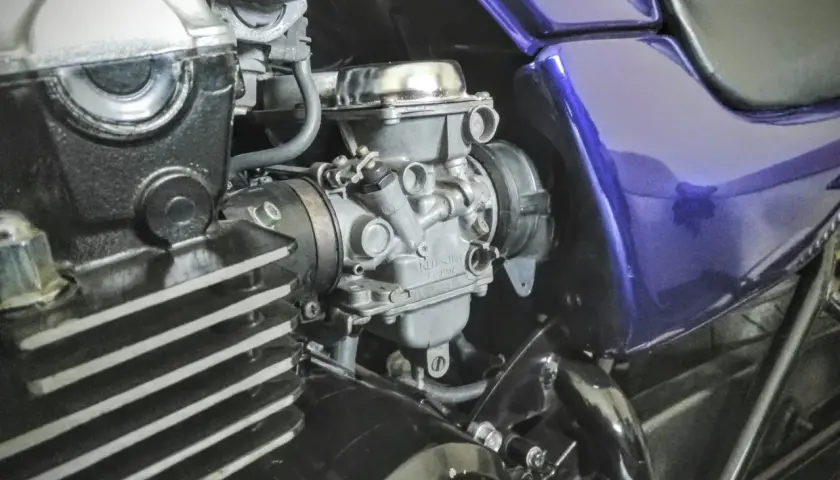 Motocyklowy gaźnik i fragment silnika z fioletowym bakiem.