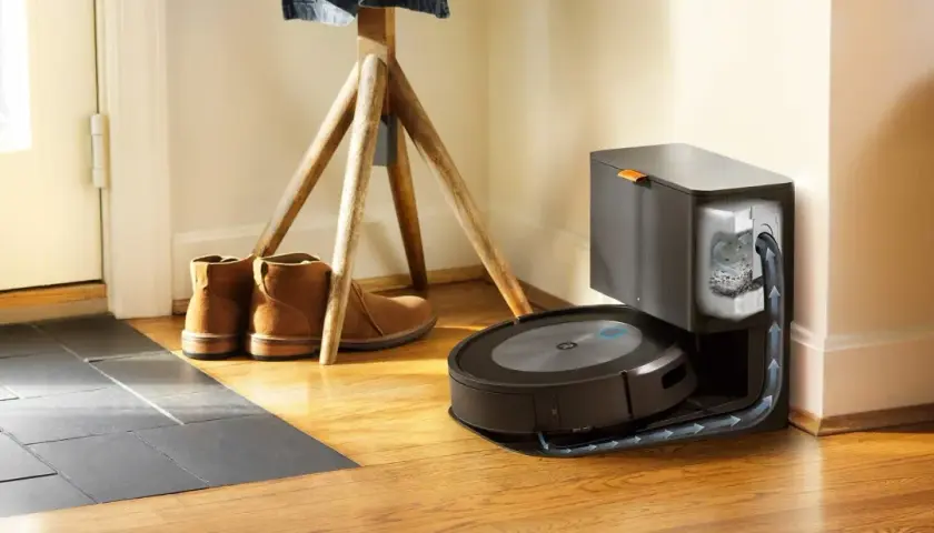 Odkurzacz iRobot Roomba na stacji dokującej, obok butów i stojaka na ubrania.