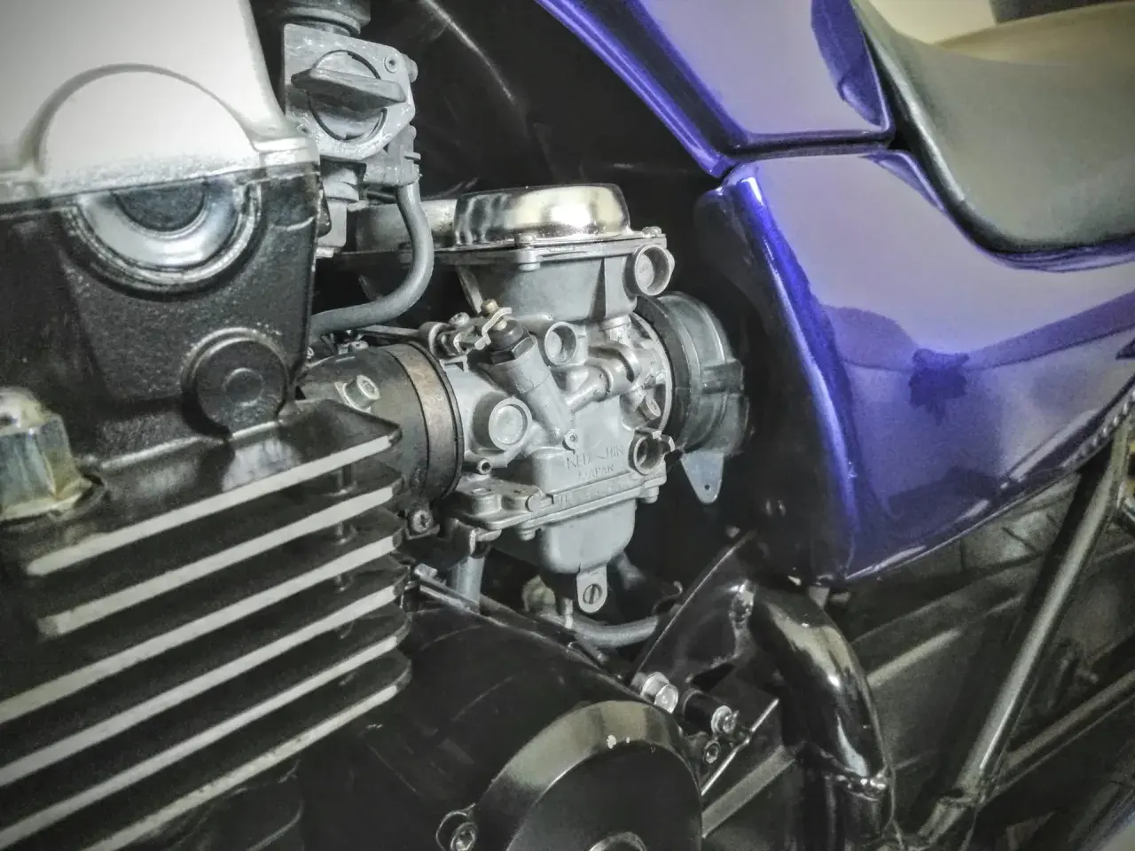 Motocyklowy gaźnik i fragment silnika z fioletowym bakiem.