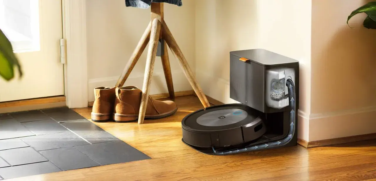 Odkurzacz iRobot Roomba na stacji dokującej, obok butów i stojaka na ubrania.